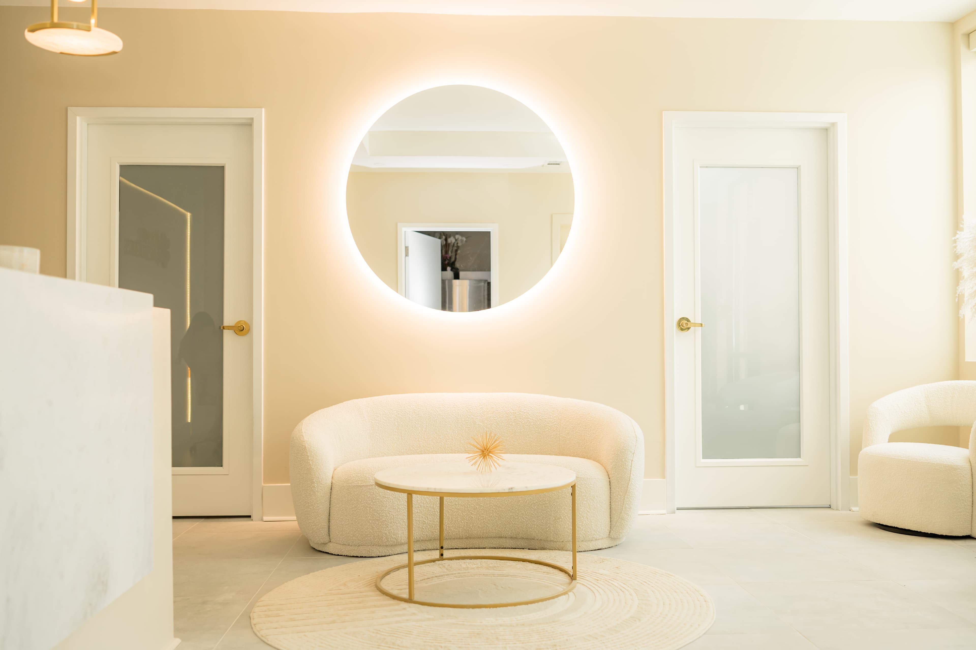 Reception lounge with bouclé sofa, halo-lit circular mirror, and honey-toned walls at La Miel Aesthetics, 7718 Six Forks Road, Raleigh, NC.